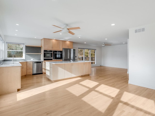 kitchen featuring a kitchen island, light brown cabinetry, ceiling fan, stainless steel appliances, and light hardwood / wood-style flooring