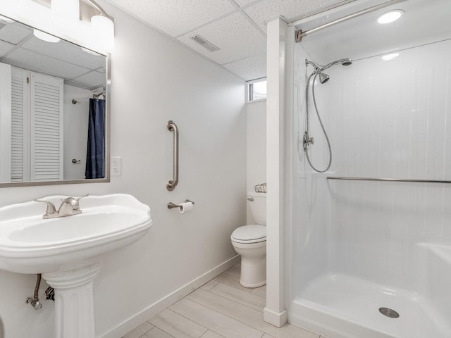 bathroom with wood-type flooring, toilet, a drop ceiling, and a shower