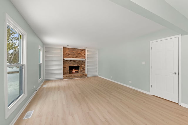 unfurnished living room featuring built in features, a brick fireplace, and light wood-type flooring