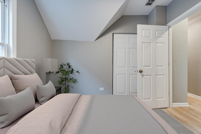 bedroom with wood-type flooring, vaulted ceiling, and a closet