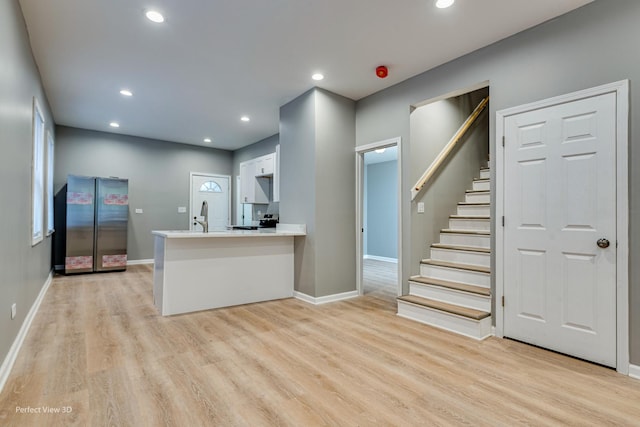 kitchen featuring stainless steel refrigerator, kitchen peninsula, light hardwood / wood-style floors, and white cabinets