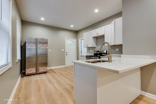 kitchen featuring sink, light hardwood / wood-style flooring, stainless steel refrigerator, white cabinetry, and kitchen peninsula