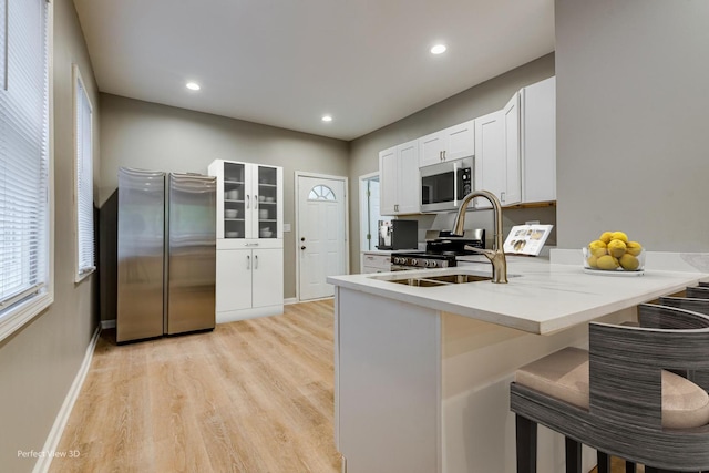 kitchen with a kitchen bar, light hardwood / wood-style flooring, kitchen peninsula, and appliances with stainless steel finishes