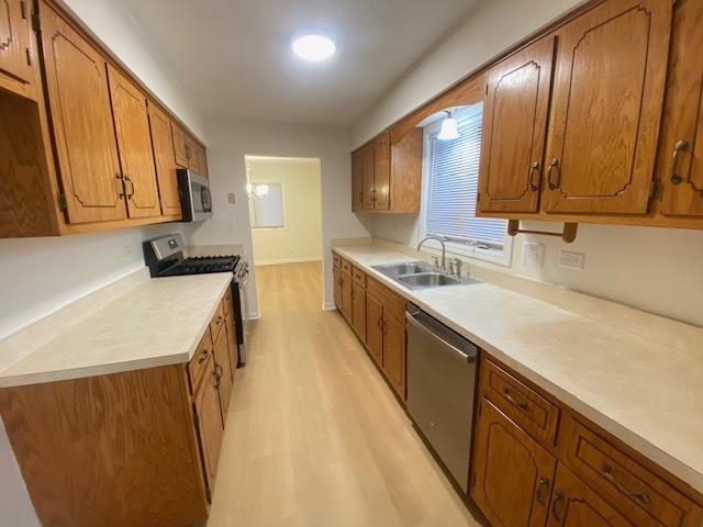 kitchen with appliances with stainless steel finishes, sink, and light wood-type flooring