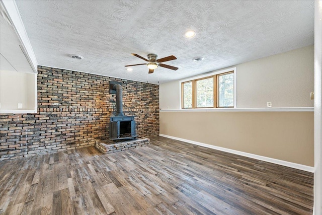 unfurnished living room with ceiling fan, dark hardwood / wood-style floors, a textured ceiling, brick wall, and a wood stove