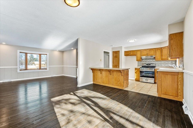 kitchen with a kitchen bar, stainless steel gas range oven, light wood-type flooring, kitchen peninsula, and backsplash