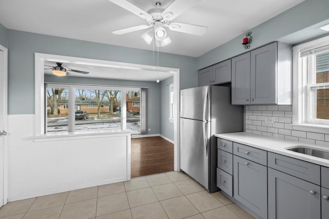 kitchen with light tile patterned flooring, sink, stainless steel refrigerator, gray cabinets, and ceiling fan