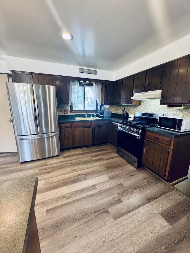 kitchen featuring sink, backsplash, dark brown cabinets, stainless steel appliances, and light wood-type flooring