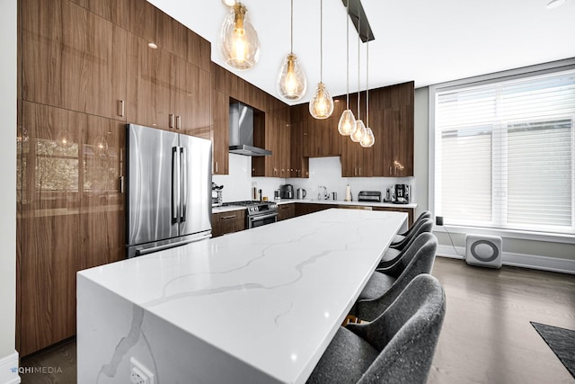 kitchen with appliances with stainless steel finishes, decorative light fixtures, a center island, light stone countertops, and wall chimney exhaust hood