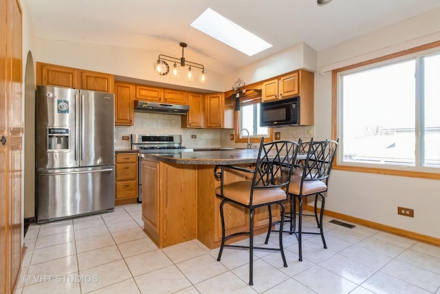 kitchen featuring light tile patterned floors, backsplash, lofted ceiling with skylight, stainless steel appliances, and a kitchen bar