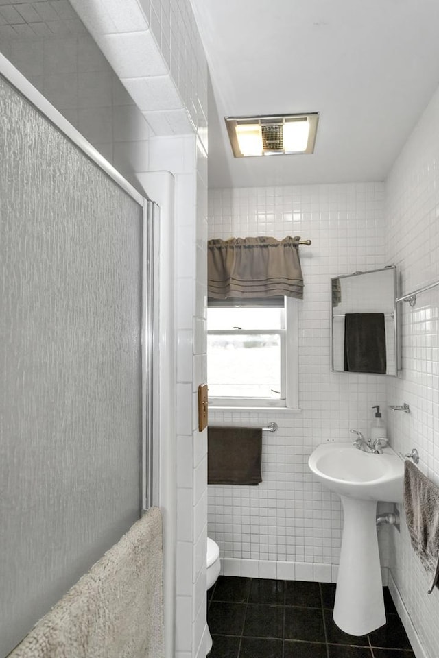 bathroom featuring tile patterned floors, toilet, a shower with door, and tile walls