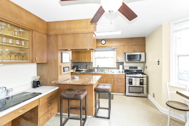 kitchen with appliances with stainless steel finishes, a kitchen breakfast bar, a kitchen island, ceiling fan, and decorative backsplash