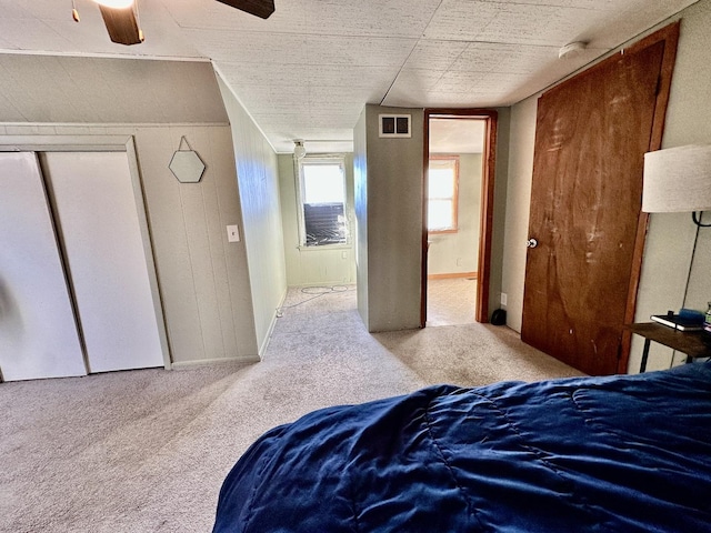 bedroom featuring wooden walls, light colored carpet, ceiling fan, and a closet