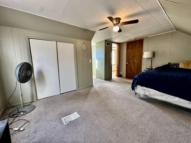 unfurnished bedroom with lofted ceiling, ceiling fan, carpet floors, a closet, and wood walls