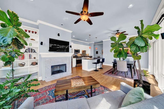 living room featuring ceiling fan, ornamental molding, a premium fireplace, and light hardwood / wood-style flooring