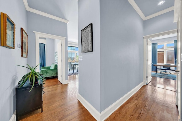 corridor with hardwood / wood-style flooring, ornamental molding, and a towering ceiling