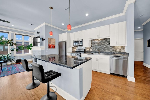 kitchen with pendant lighting, appliances with stainless steel finishes, white cabinetry, light hardwood / wood-style floors, and dark stone counters