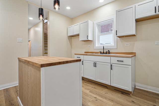 kitchen featuring pendant lighting, white cabinetry, sink, butcher block counters, and light hardwood / wood-style flooring