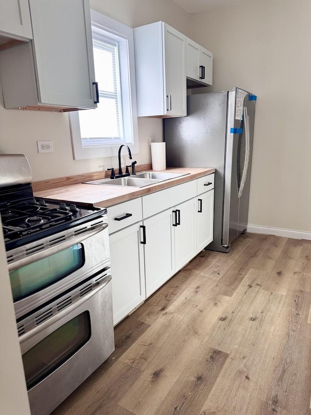 kitchen with butcher block countertops, sink, stainless steel appliances, light hardwood / wood-style floors, and white cabinets