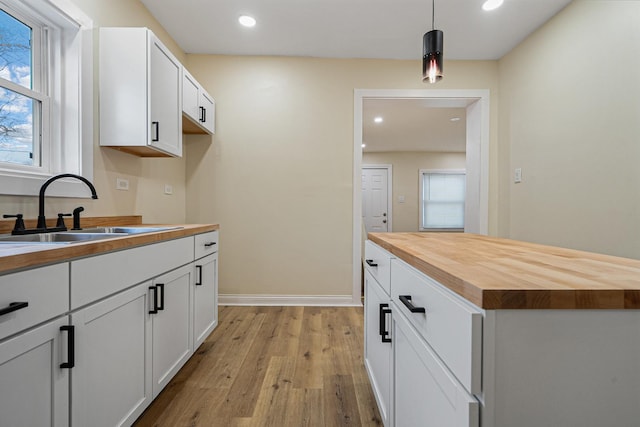 kitchen with white cabinetry, sink, decorative light fixtures, and wooden counters