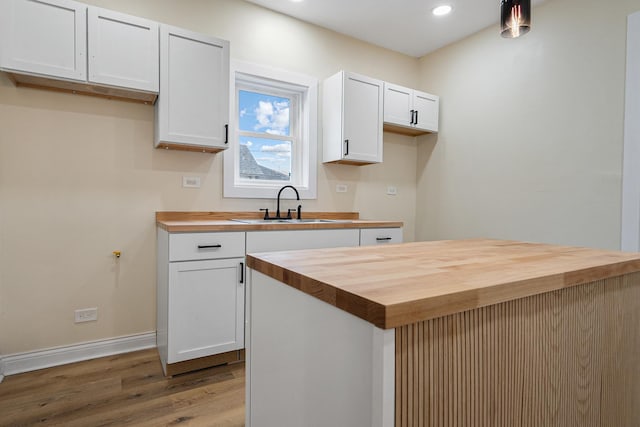 kitchen with sink, wooden counters, white cabinetry, hardwood / wood-style floors, and a center island