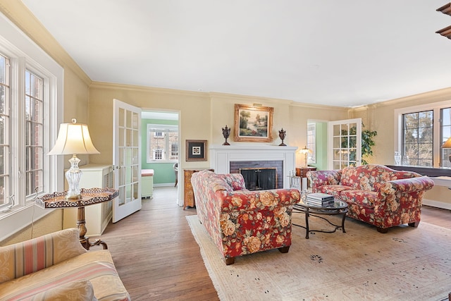 living room featuring a brick fireplace, light hardwood / wood-style flooring, ornamental molding, and french doors