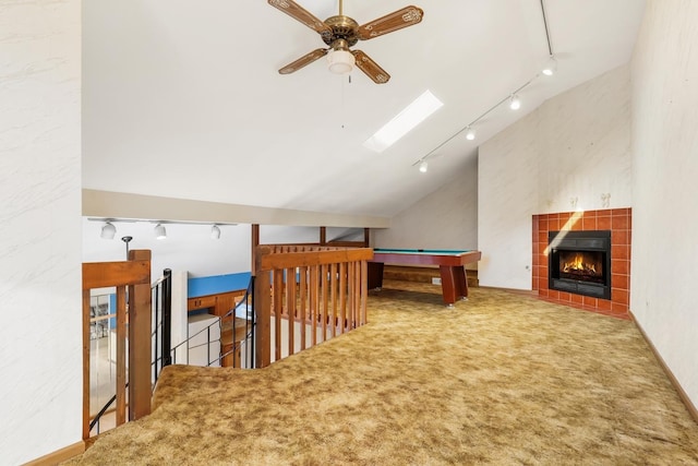 interior space with vaulted ceiling with skylight, a fireplace, carpet flooring, ceiling fan, and track lighting