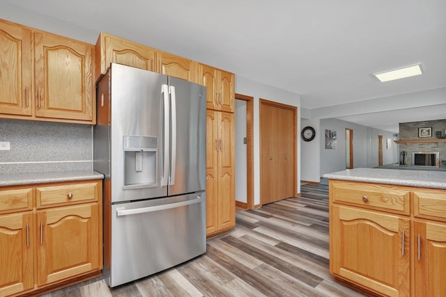 kitchen with tasteful backsplash, light wood-type flooring, a large fireplace, and stainless steel refrigerator with ice dispenser