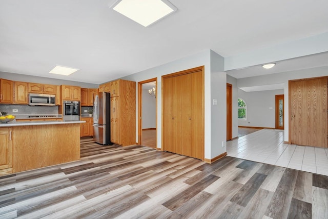 kitchen with tasteful backsplash, appliances with stainless steel finishes, kitchen peninsula, and light hardwood / wood-style floors