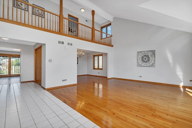 unfurnished living room featuring beam ceiling, high vaulted ceiling, light wood-type flooring, and an inviting chandelier