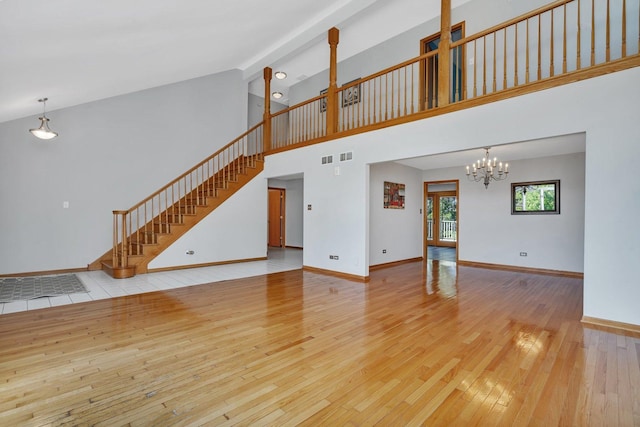 unfurnished living room featuring an inviting chandelier, light hardwood / wood-style floors, and a high ceiling