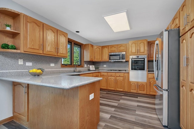 kitchen featuring sink, light hardwood / wood-style flooring, appliances with stainless steel finishes, decorative backsplash, and kitchen peninsula