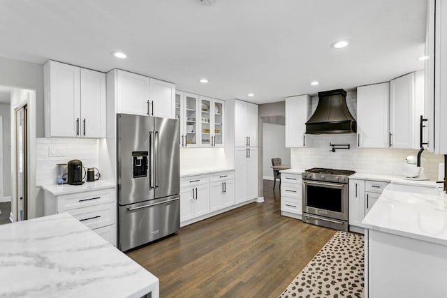 kitchen featuring light stone counters, custom exhaust hood, stainless steel appliances, and white cabinets