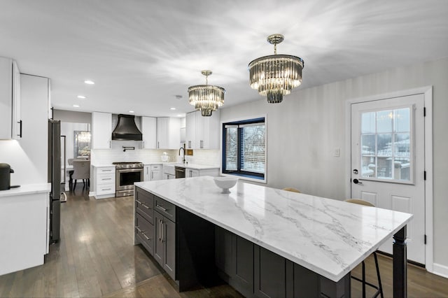 kitchen with appliances with stainless steel finishes, white cabinetry, hanging light fixtures, light stone counters, and custom exhaust hood