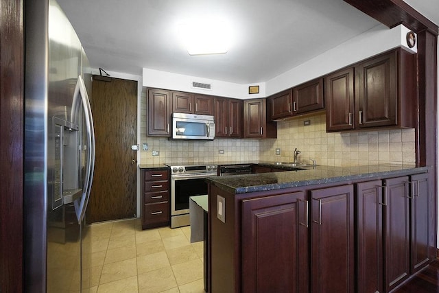 kitchen with sink, dark stone counters, kitchen peninsula, stainless steel appliances, and decorative backsplash