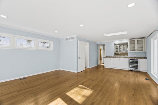 unfurnished living room with wine cooler, hardwood / wood-style floors, crown molding, and a wealth of natural light