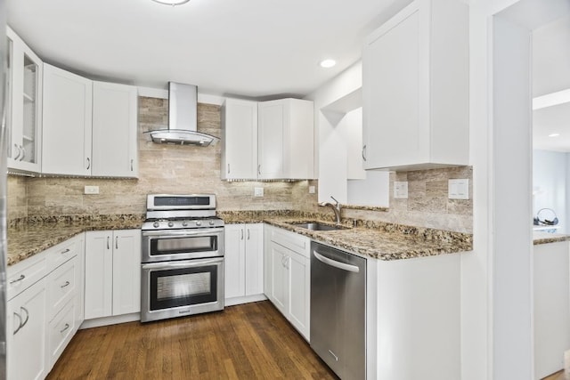 kitchen with sink, appliances with stainless steel finishes, white cabinetry, stone countertops, and wall chimney exhaust hood