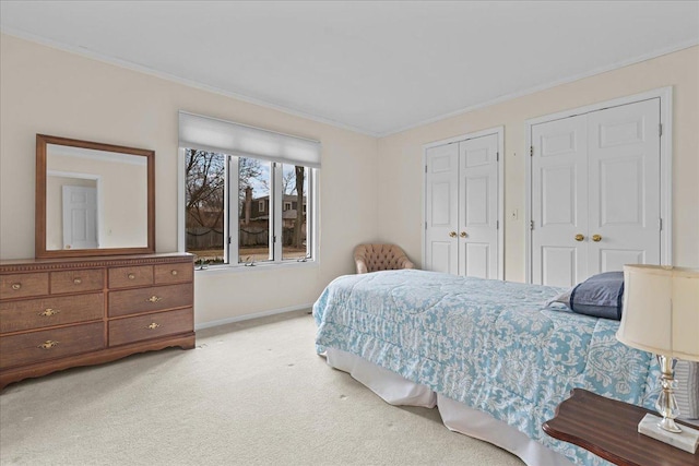 bedroom with crown molding, two closets, and light colored carpet