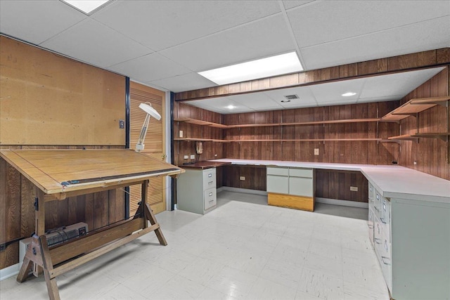 office space with a drop ceiling, built in desk, and wooden walls