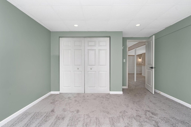 unfurnished bedroom with a drop ceiling, light colored carpet, and a closet