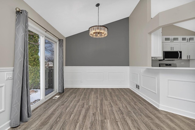 unfurnished dining area with an inviting chandelier, dark wood-type flooring, and vaulted ceiling