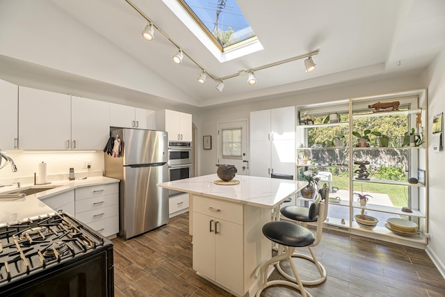 kitchen featuring lofted ceiling with skylight, sink, appliances with stainless steel finishes, a kitchen island, and white cabinets