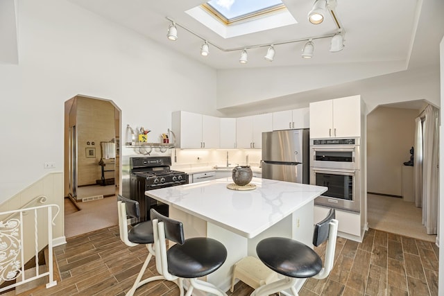 kitchen featuring sink, appliances with stainless steel finishes, a skylight, white cabinets, and a kitchen island