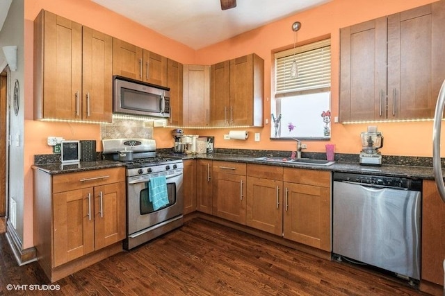 kitchen with appliances with stainless steel finishes, dark hardwood / wood-style floors, decorative light fixtures, sink, and dark stone countertops