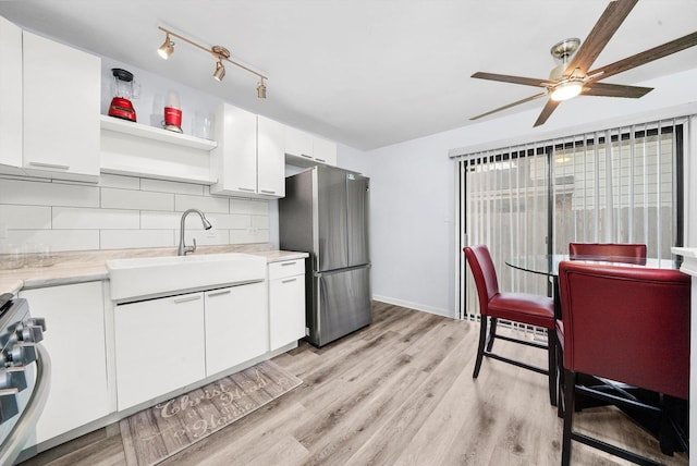 kitchen with sink, white cabinetry, light wood-type flooring, stainless steel appliances, and decorative backsplash