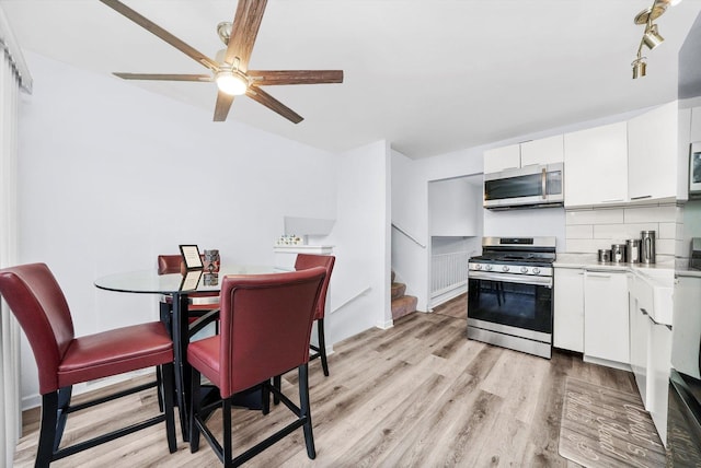 kitchen with appliances with stainless steel finishes, tasteful backsplash, white cabinetry, ceiling fan, and light hardwood / wood-style flooring