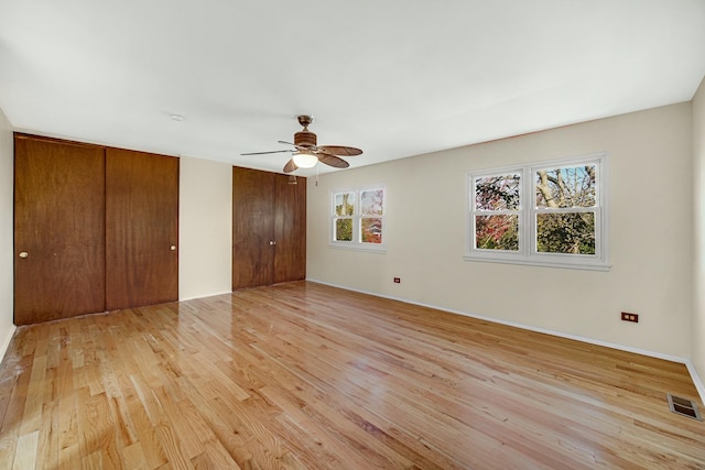 unfurnished bedroom featuring two closets, light hardwood / wood-style flooring, and ceiling fan