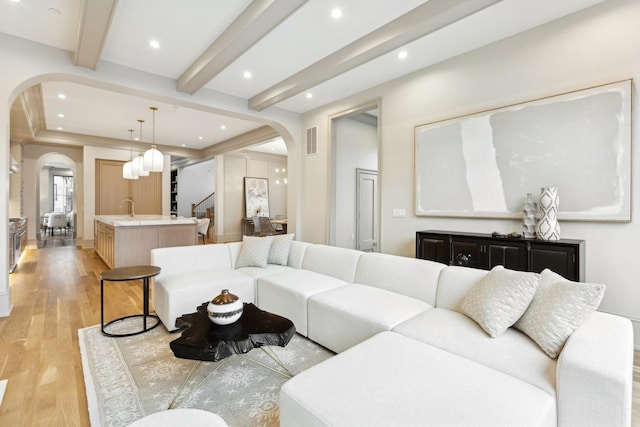 living room with beam ceiling, sink, and light hardwood / wood-style floors