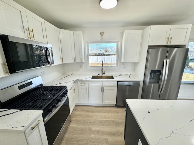 kitchen featuring sink, white cabinetry, light stone counters, light hardwood / wood-style flooring, and appliances with stainless steel finishes