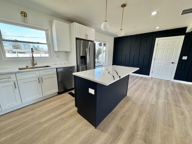 kitchen with sink, appliances with stainless steel finishes, white cabinetry, a center island, and decorative light fixtures